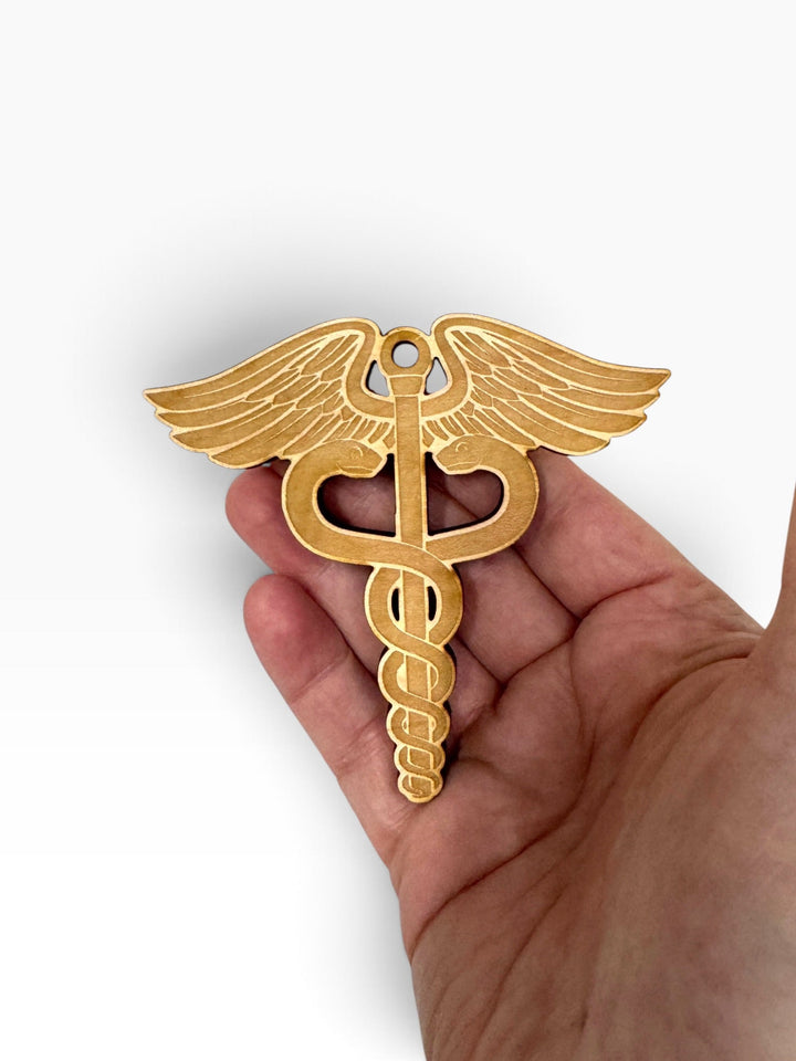 HipFlaskPlus laser-engraved wooden medical caduceus ornament held in a hand, featuring rustic cedar wood detail.