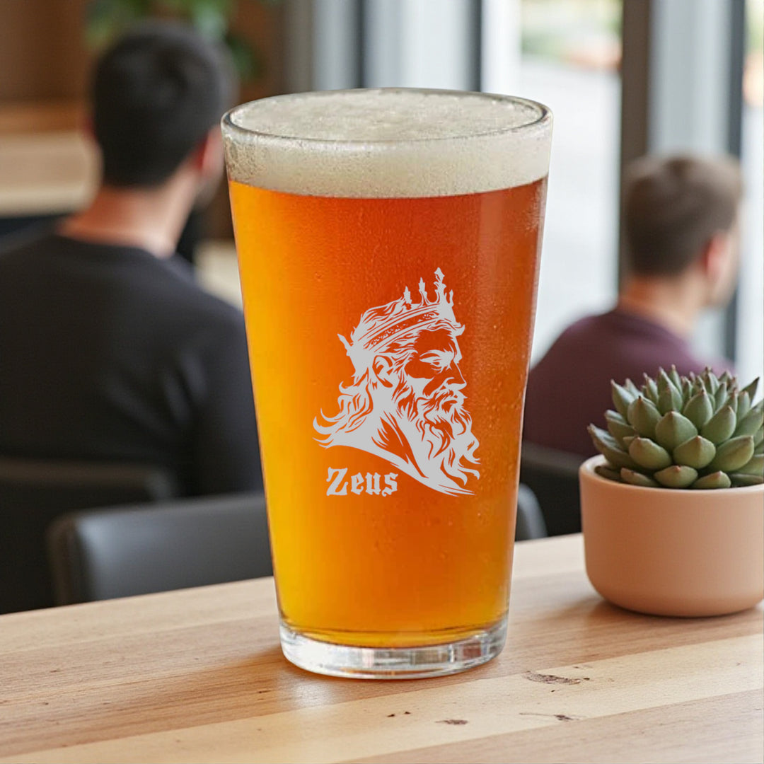 HipFlaskPlus 16oz pint beer glass filled with beer engraved with Zeus God of Thunder on a table in a pub