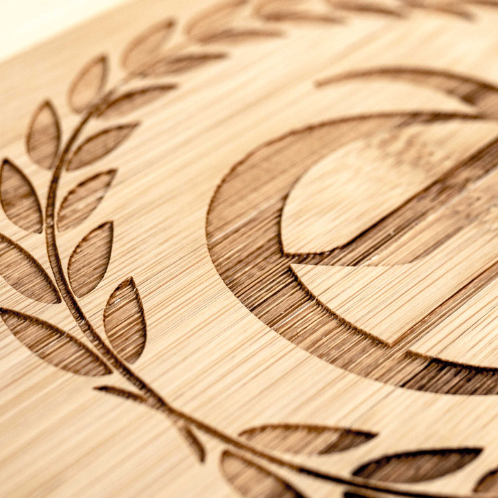 HipFlaskPlus bamboo cutting board engraved with a personalized initial in a laurel wreath, close-up of the engraving