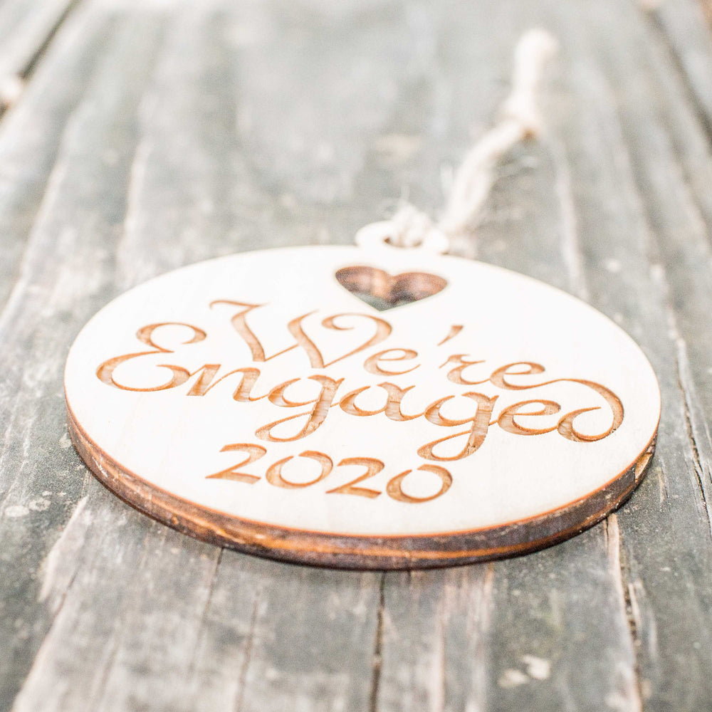 HipFlaskPlus raw wood We're Engaged 2020 ornament on rustic wood, angled view