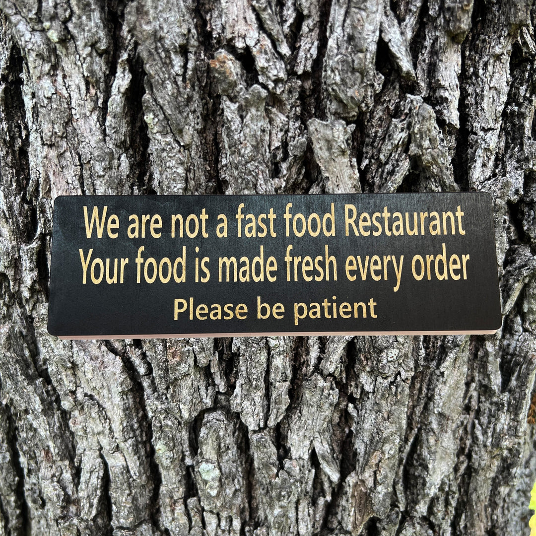 HipFlaskPlus custom We Are Not a Fast Food Restaurant Please Be Patient sign in black on a tree trunk