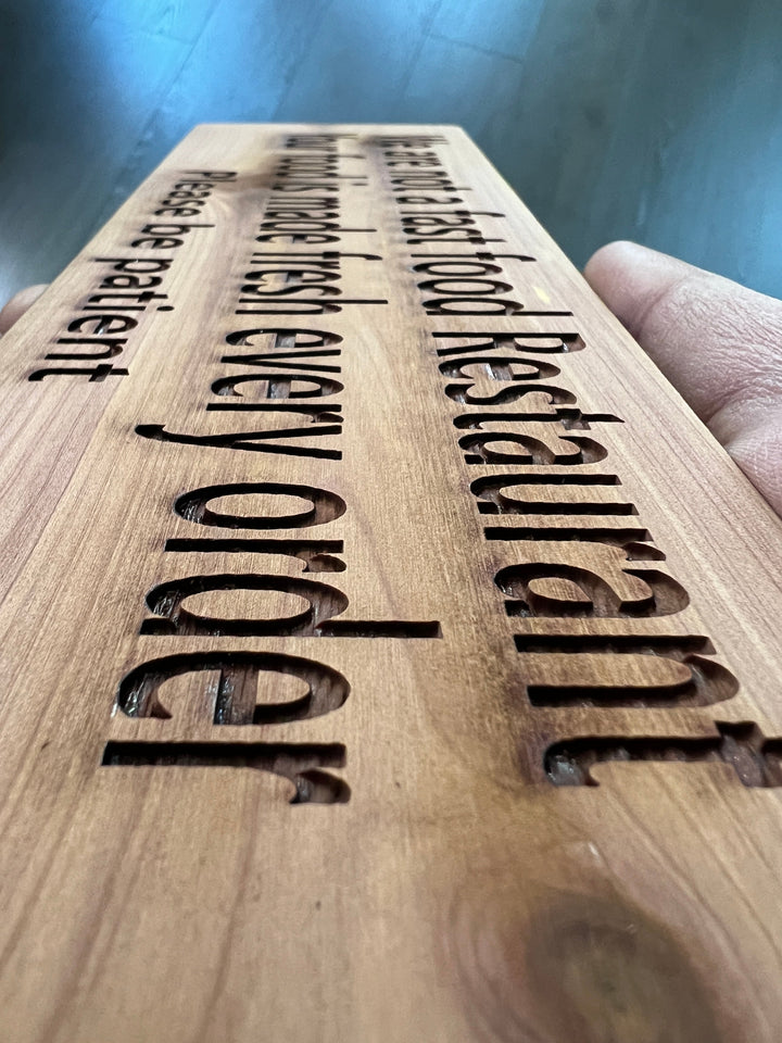 HipFlaskPlus custom We Are Not a Fast Food Restaurant Please Be Patient sign in an angled close-up of the cedar