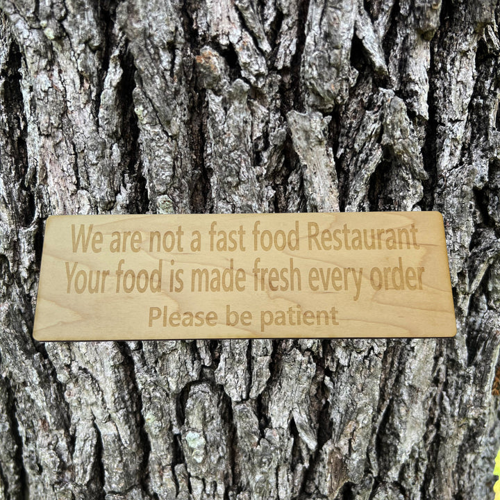 HipFlaskPlus custom We Are Not a Fast Food Restaurant Please Be Patient sign on a tree trunk
