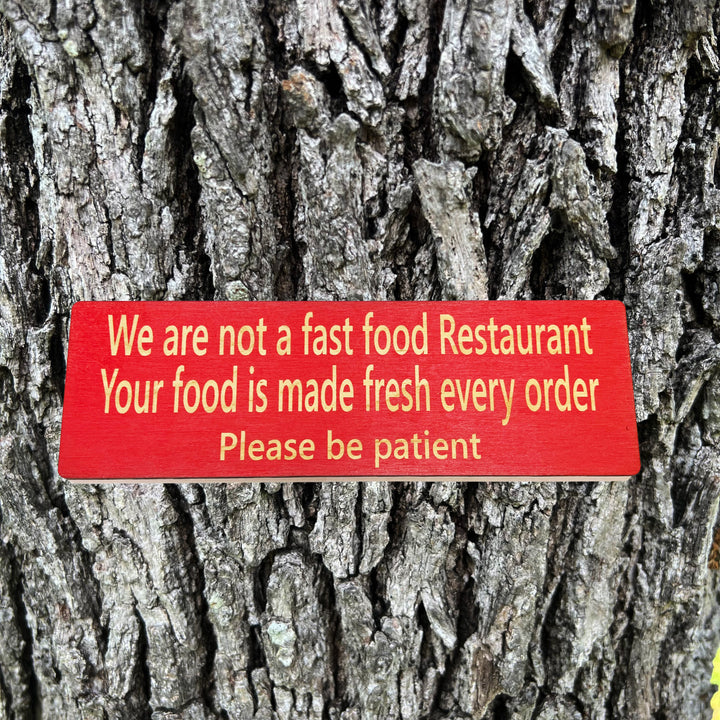 HipFlaskPlus custom We Are Not a Fast Food Restaurant Please Be Patient sign in red on a tree trunk