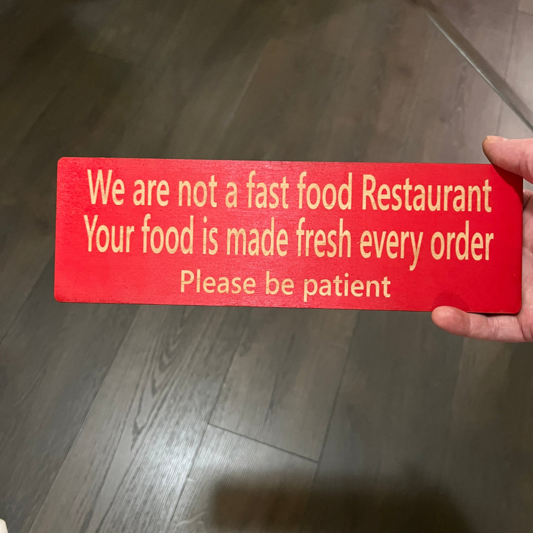 Hand holding a HipFlaskPlus custom We Are Not a Fast Food Restaurant Please Be Patient sign in red