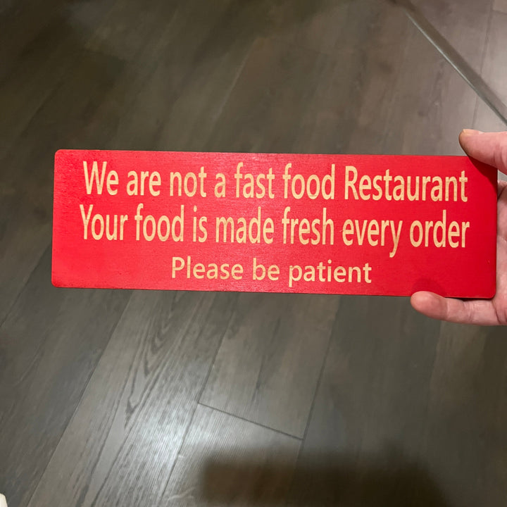 Hand holding a HipFlaskPlus custom We Are Not a Fast Food Restaurant Please Be Patient sign in red